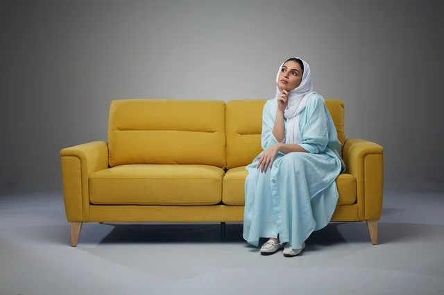 Saudi Woman in Blue Abaya Thinking on Yellow Sofa Studio