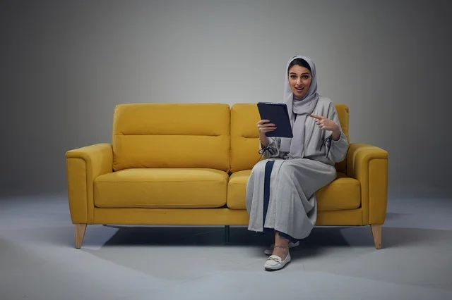 امرأة سعودية تجلس على أريكة تستخدم جهازًا لوحيًا