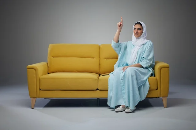 امرأة سعودية تشير للأعلى تجلس على أريكة صفراء امرأة سعودية تشير للأعلى تجلس على أريكة صفراء
