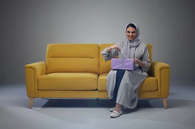 Saudi Woman Opening Purple Gift Box on Yellow Sofa