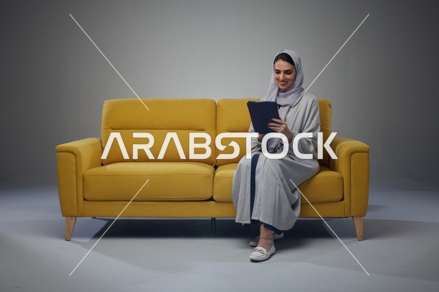 امرأة سعودية تستخدم جهاز لوحي على أريكة صفراء