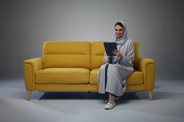 Saudi Woman Using Digital Tablet on Yellow Sofa Saudi Woman Using Digital Tablet on Yellow Sofa