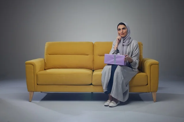Saudi Woman on Yellow Sofa Holding a Purple Gift Box
