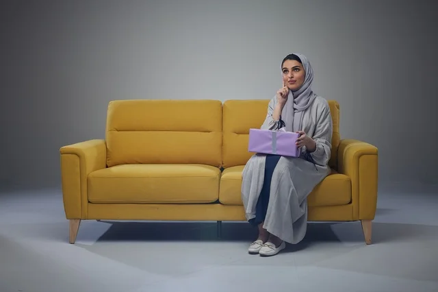امرأة سعودية على أريكة صفراء تحمل صندوق هدايا