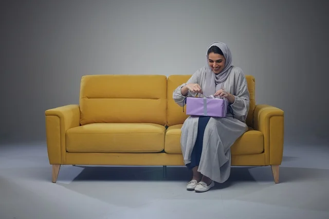 Saudi Woman Opening Gift on Yellow Sofa Saudi Woman Opening Gift on Yellow Sofa