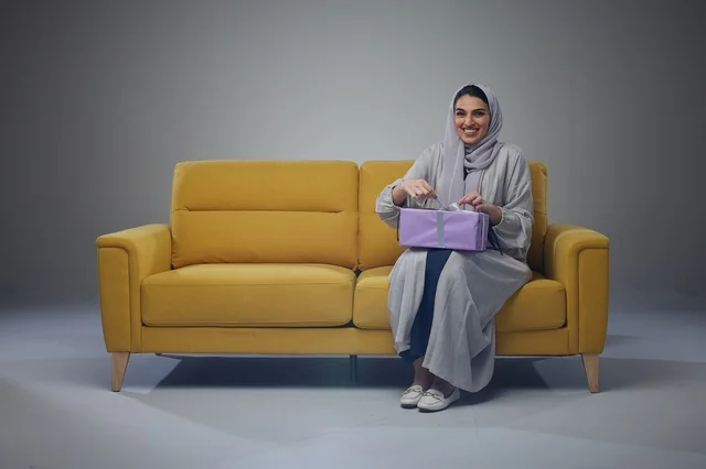 امرأة سعودية مع صندوق هدايا على أريكة صفراء