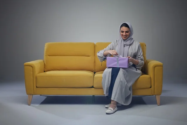 Saudi Woman Holding Purple Gift Box on Yellow Sofa