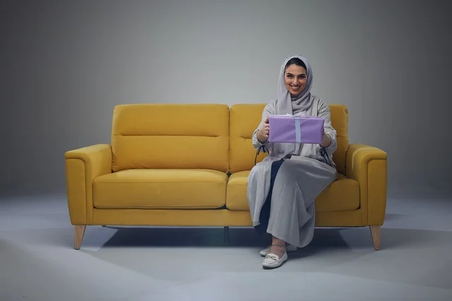 امرأة سعودية تحمل صندوق هدايا على أريكة صفراء