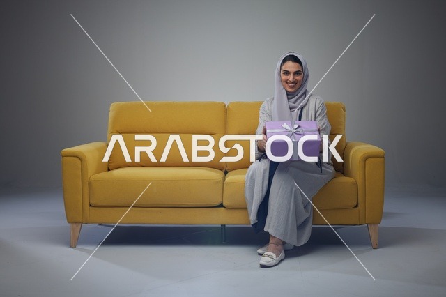 Saudi Woman on Yellow Sofa Holding Purple Gift Box - Photo