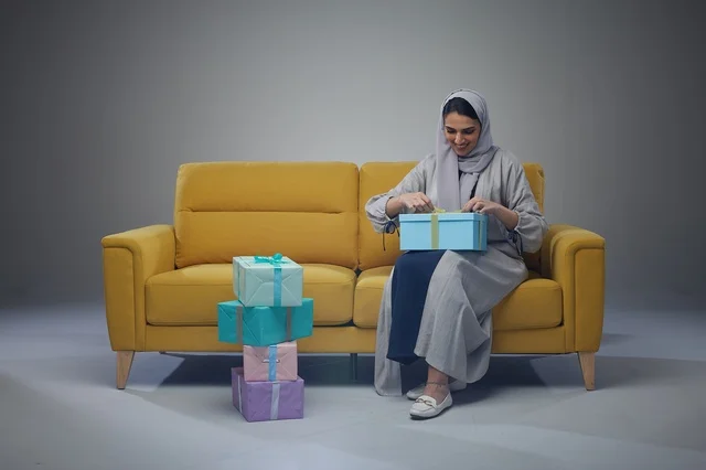 امرأة سعودية تجلس على أريكة صفراء مع صناديق هدايا