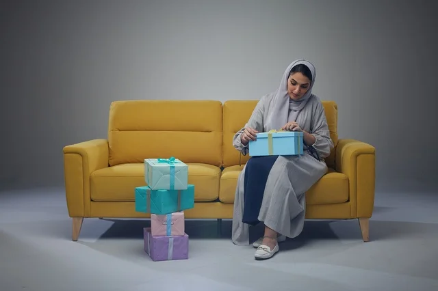 امرأة سعودية تجلس على أريكة صفراء تحمل علب هدايا
