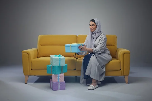 امرأة سعودية على أريكة صفراء مع صناديق هدايا ملونة