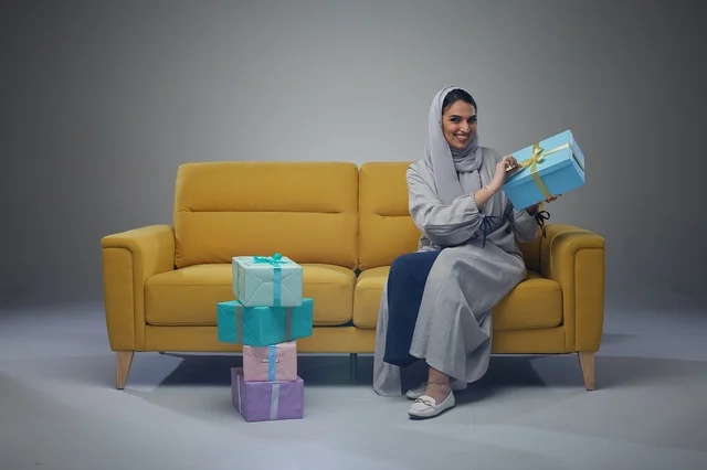 Saudi Woman Holding Gift Boxes Sitting on Yellow Sofa