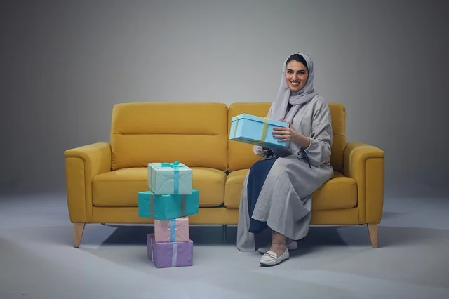 امرأة سعودية تجلس على أريكة صفراء مع صناديق هدايا