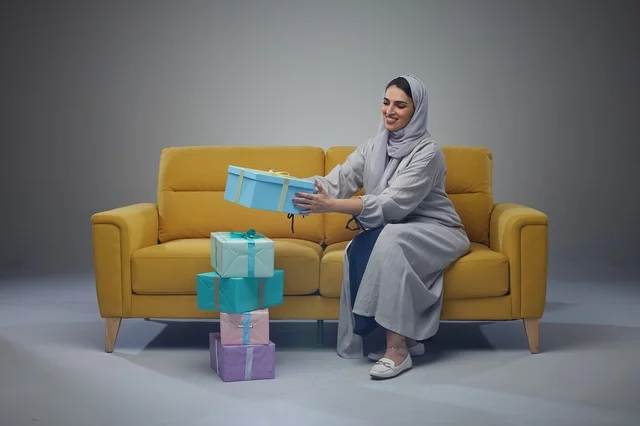 Saudi Woman on Yellow Sofa Holding Colorful Gift Boxes
