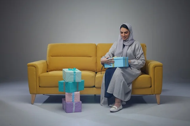 Saudi Woman Wearing Abaya on Yellow Sofa Holding Gift Boxes