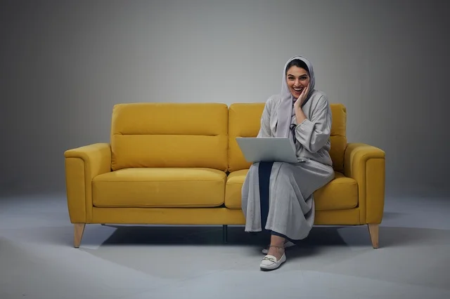 امرأة سعودية تستخدم الكمبيوتر المحمول على أريكة صفراء امرأة سعودية تستخدم الكمبيوتر المحمول على أريكة صفراء