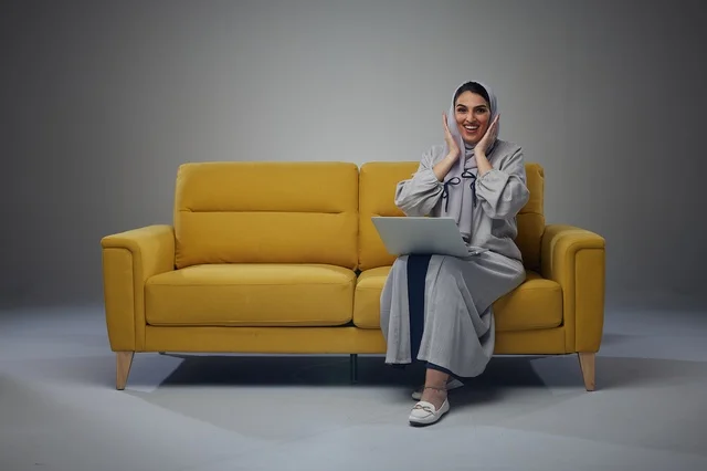 امرأة سعودية مع حاسوب محمول على أريكة صفراء