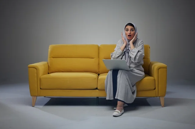 Saudi Woman Using Laptop on Yellow Sofa Surprise