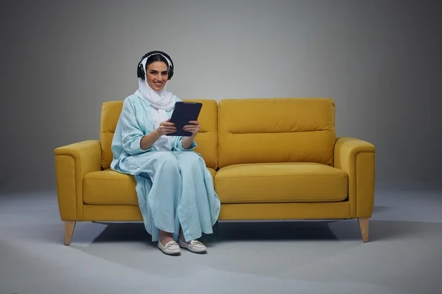 امرأة سعودية في استوديو مع أريكة صفراء وجهاز لوحي