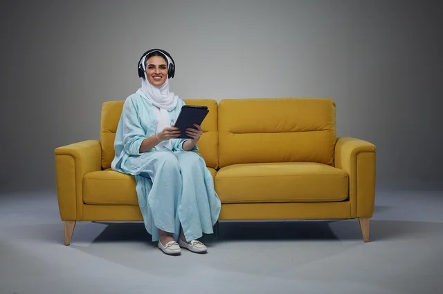 Saudi Woman on Yellow Sofa with Tablet and Headphones