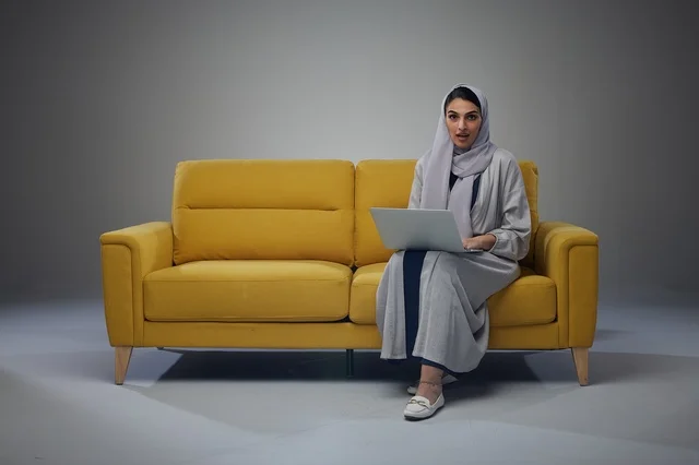 امرأة سعودية تستخدم الحاسوب المحمول على أريكة صفراء