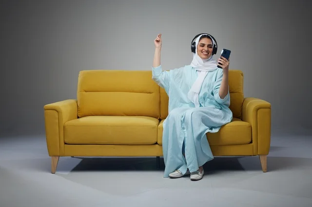 Saudi Woman with Headphones on Yellow Sofa