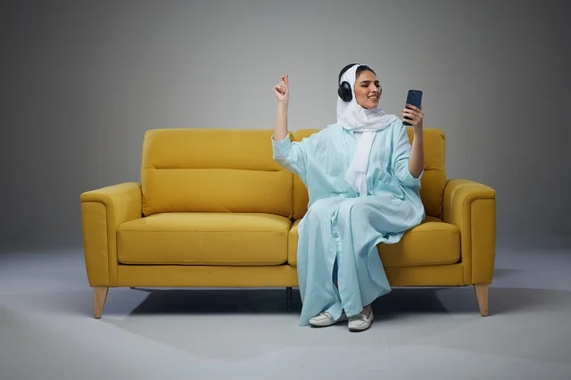 Saudi Woman Sitting on Sofa Using Tablet with Headphones