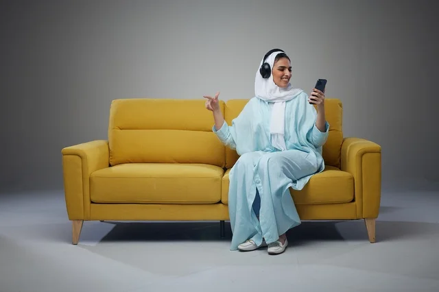 Saudi Woman Sitting on Sofa Using Tablet with Headphones