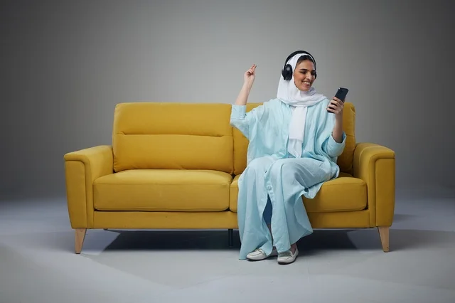 Saudi Woman Sitting on Sofa Using Tablet with Headphones