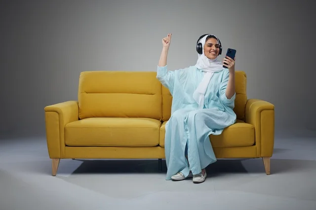 Saudi Woman with Headphones and Smartphone on Sofa