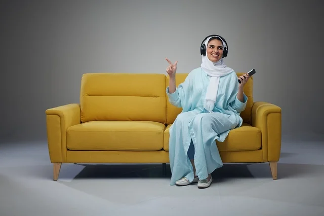 Saudi Woman Using Headphones on Yellow Sofa Studio