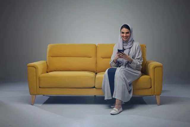 امرأة سعودية تستخدم الهاتف الذكي على أريكة صفراء