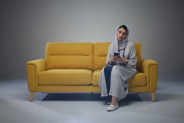 Saudi Woman on Yellow Sofa Using Smartphone in Studio