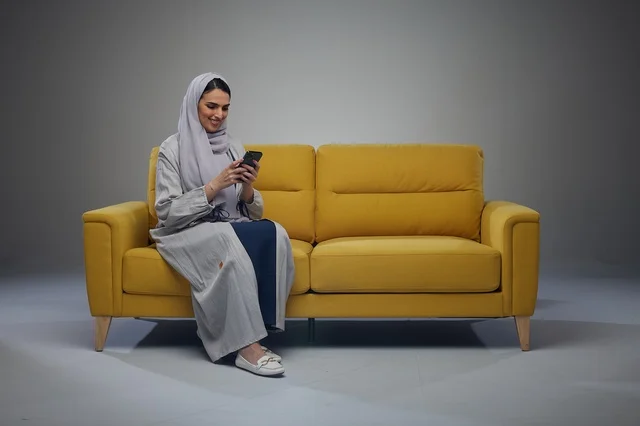 Saudi Woman on Yellow Sofa Using Smartphone in Studio