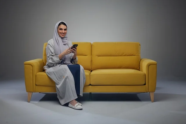 Saudi Woman Using Smartphone on Yellow Sofa in Studio