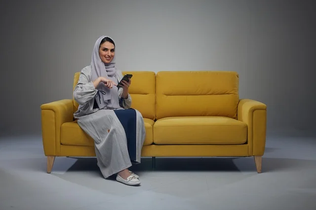 Saudi Woman on Yellow Sofa Using Smartphone in Studio