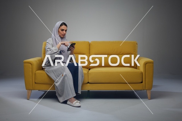 امرأة سعودية تستخدم هاتف ذكي على أريكة صفراء