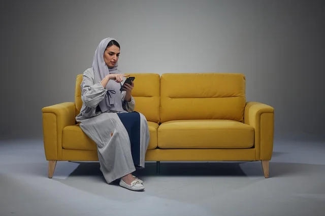 Saudi Woman Using Smartphone on Yellow Sofa in Studio
