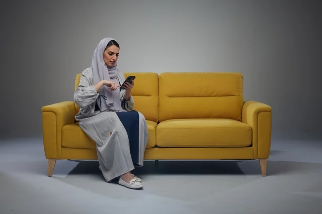 Saudi Woman Using Smartphone on Yellow Sofa in Studio