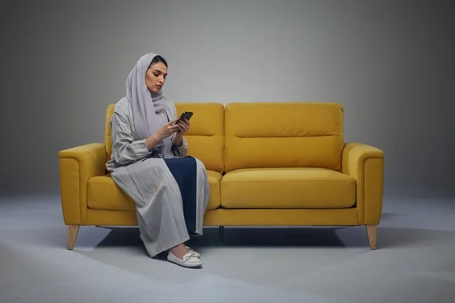 Saudi Woman on Yellow Sofa Using Smartphone in Studio