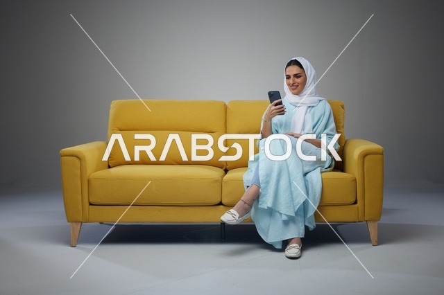 امرأة سعودية تستخدم الهاتف الذكي على أريكة صفراء