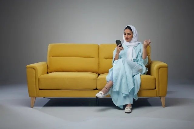 Saudi Woman Using Smartphone on Yellow Sofa
