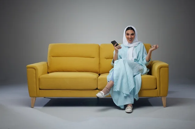 امرأة سعودية على أريكة صفراء تستخدم الهاتف الذكي