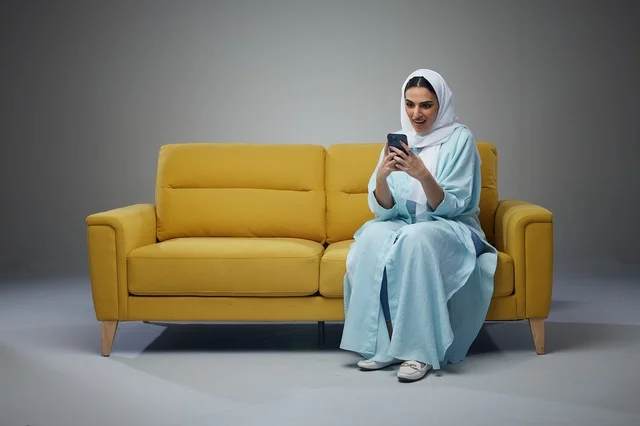Saudi Woman on Yellow Sofa Using Smartphone in Studio