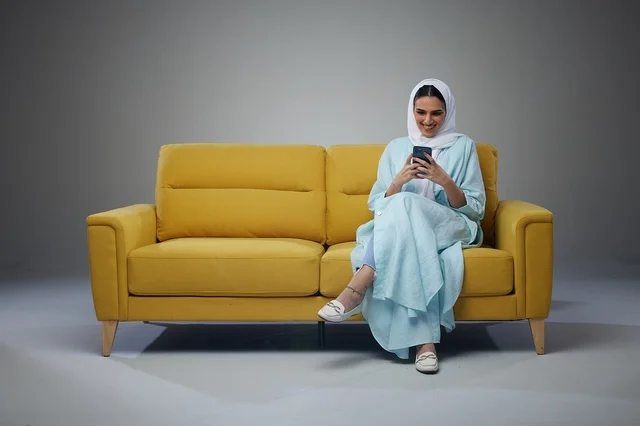 امرأة سعودية تستخدم الهاتف الذكي على أريكة صفراء