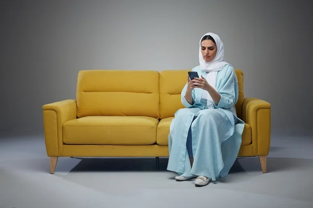 Saudi Woman on Yellow Sofa Using Smartphone in Studio