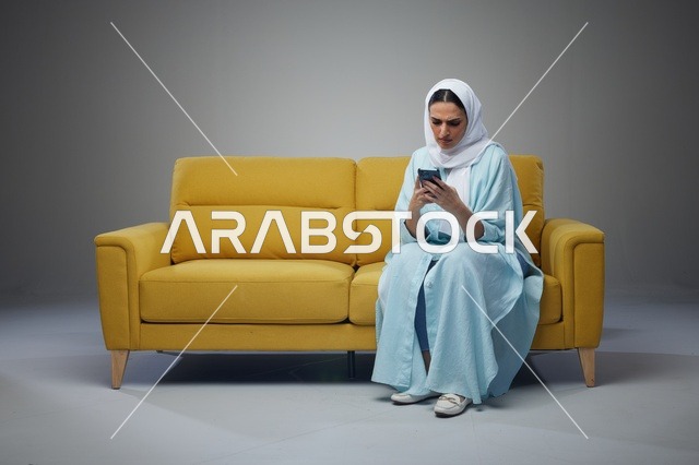 امرأة سعودية تستخدم الهاتف الذكي على أريكة صفراء