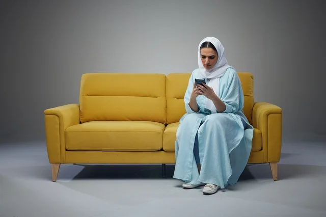 Saudi Woman Using Smartphone on Yellow Sofa in Studio