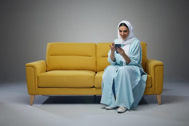 Saudi Woman on Yellow Sofa Using Smartphone Studio Shot